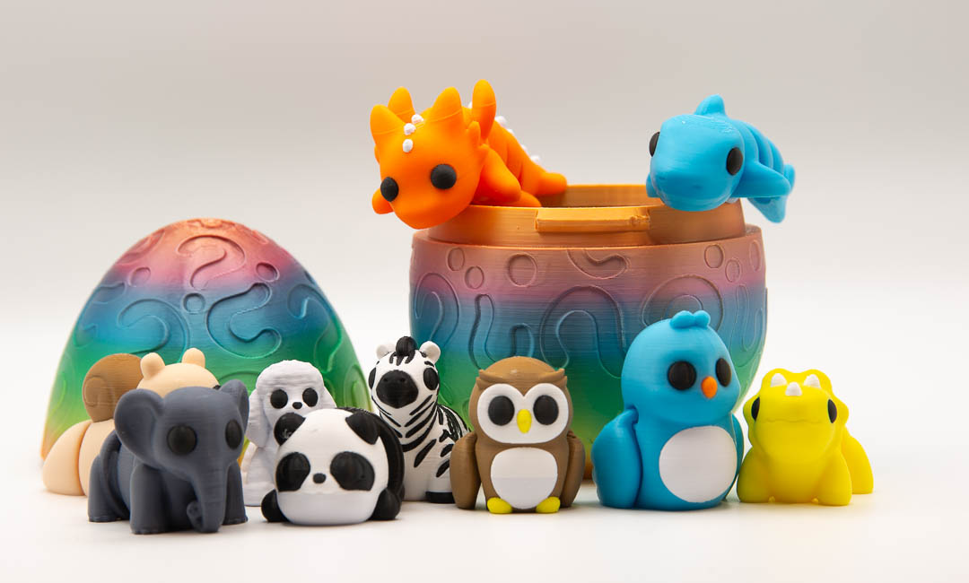 Rainbow mystery egg surrounded by 3D printed flexi animals